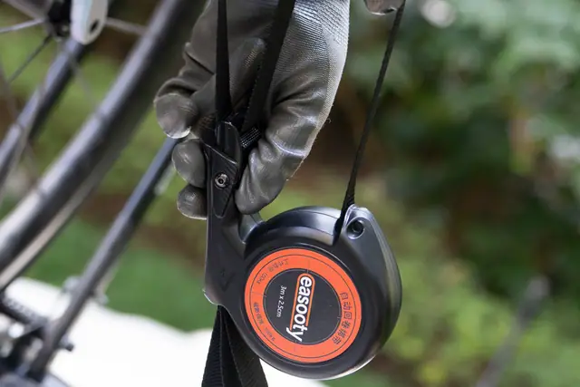 Hand tensioning a black webbing strap through an auto-retract reel beside a bicycle