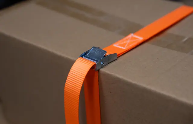 Cam buckle strap tightened over the edge of a cardboard box