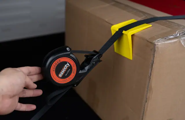 Yellow ABS corner protector on a carton with an auto-retract strap threaded through it