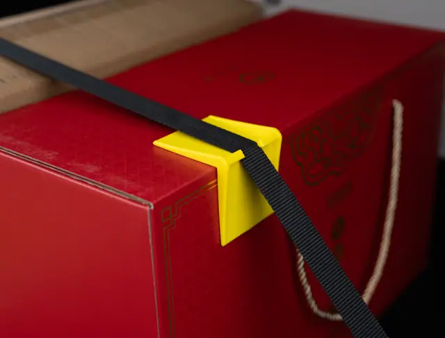 Yellow ABS corner protector on a red box corner with a black strap threaded through its slot