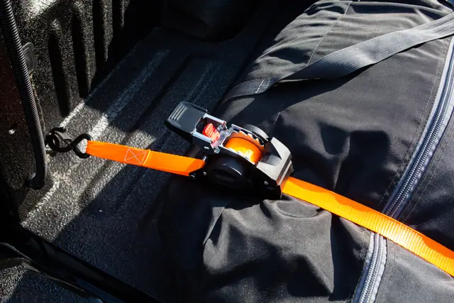 Self-retracting ratchet strap hooked to a pickup bed rail, holding a soft bag in place