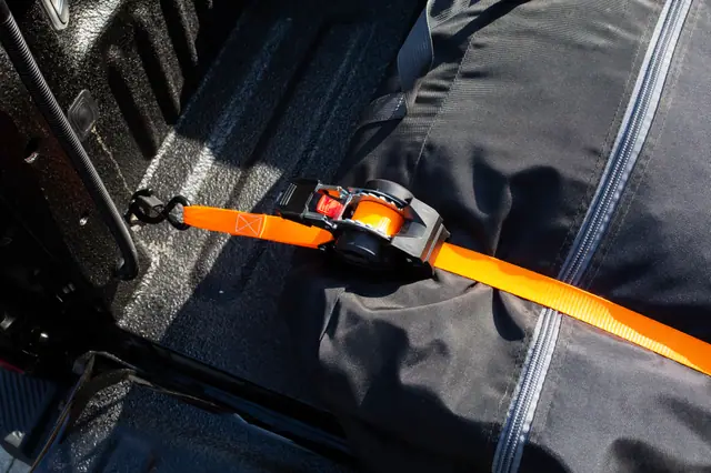 Self-retracting ratchet strap tensioned over a covered load in a truck bed