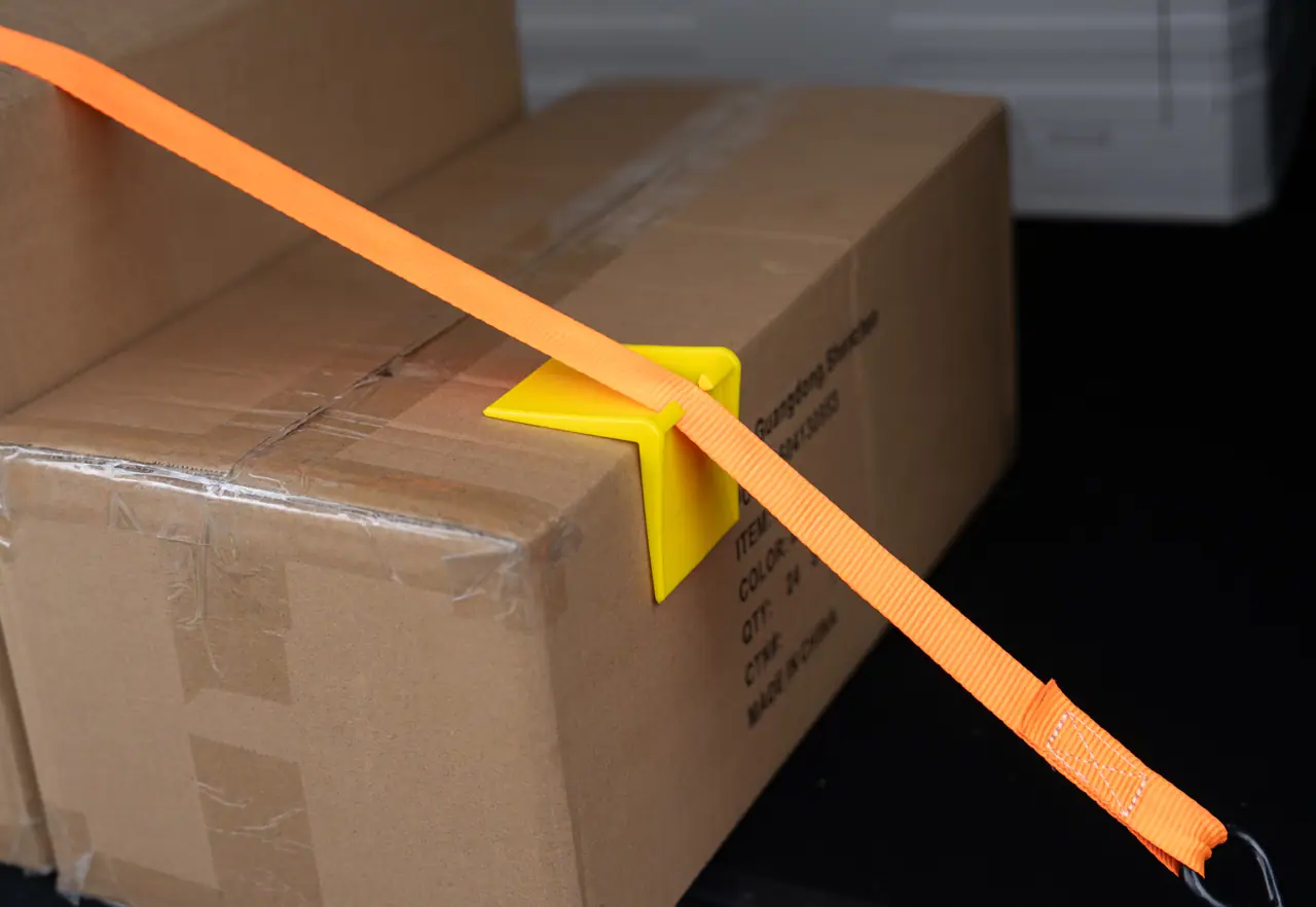 Carton in a warehouse secured with a strap threaded through a yellow ABS corner protector